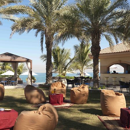 Al Raha Beach Resort & Spa Абу Даби Ресторант снимка The photo depicts a beautiful outdoor setting with several elements of relaxation and leisure. In the foreground, there are large, comfortable bean bag chairs arranged on a grassy area, accompanied by low tables. Surrounding this seating area are tal
