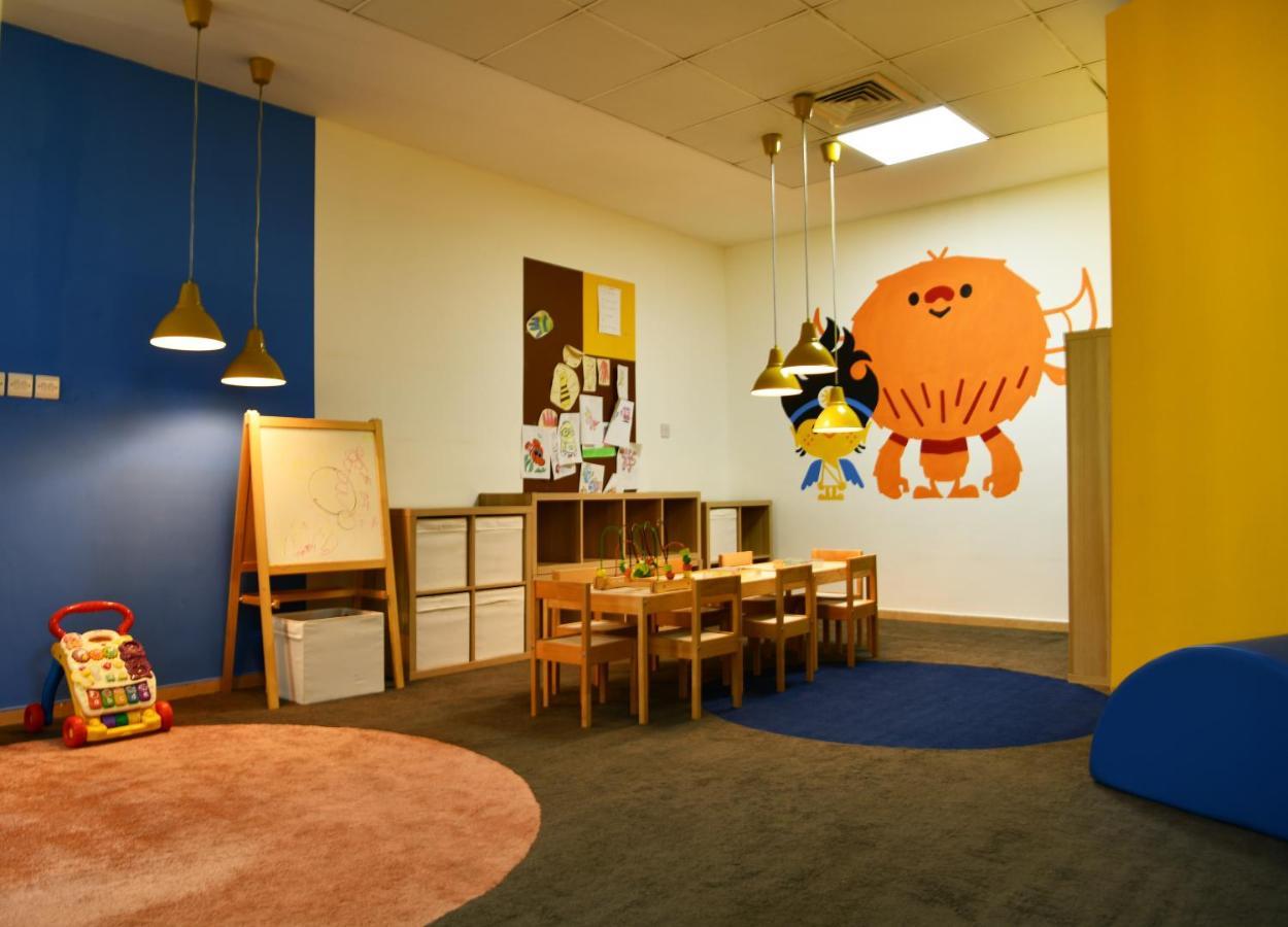 Al Raha Beach Resort & Spa Абу Даби Екстериор снимка The photo shows a colorful children's classroom or play area. The walls are painted in various shades, including blue and yellow. There is a large, playful character mural on one wall that appears to be a friendly monster. 

In the room, there is a s