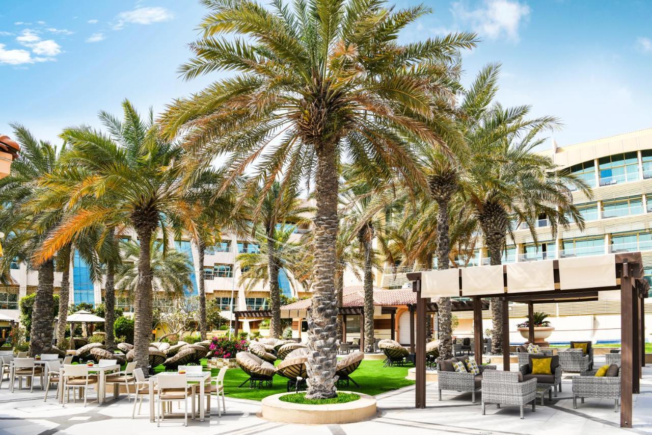 Al Raha Beach Resort & Spa Абу Даби Екстериор снимка The photo shows a picturesque outdoor area, likely at a resort or hotel. It features several tall palm trees that provide a tropical feel. In the foreground, there are several lounge chairs and seating arrangements, suggesting a relaxing environment.