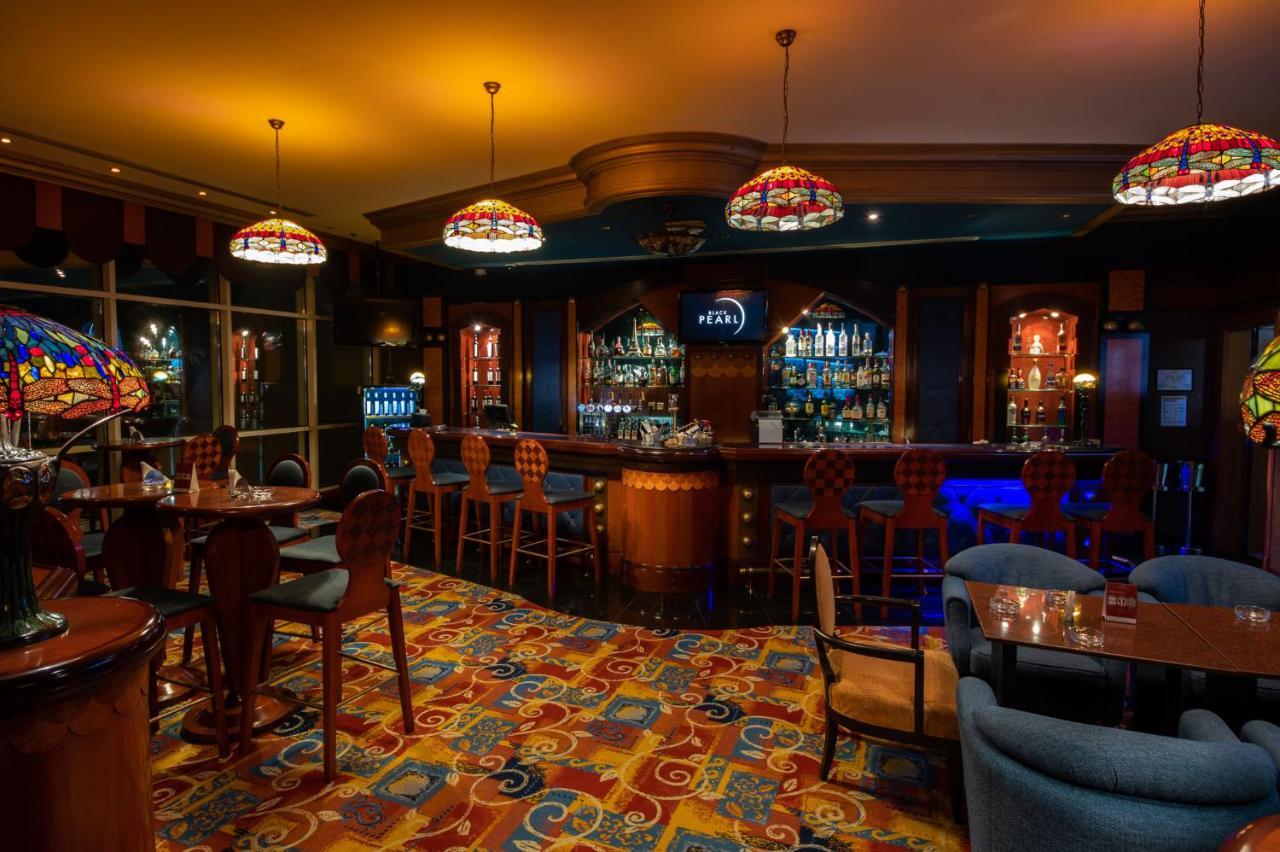 Al Raha Beach Resort & Spa Абу Даби Екстериор снимка The photo shows a cozy bar interior, featuring a well-stocked bar area with various bottles displayed on shelves. The bar is illuminated by colorful stained glass light fixtures, creating a warm and inviting atmosphere. The floor is covered with a vi