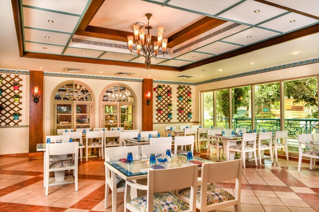 Al Raha Beach Resort & Spa Абу Даби Екстериор снимка The photo shows the interior of a restaurant or dining area. The space has a warm and inviting atmosphere, featuring a mix of decorative elements. 

- **Seating**: There are several white wooden tables and chairs arranged throughout the area, some wi