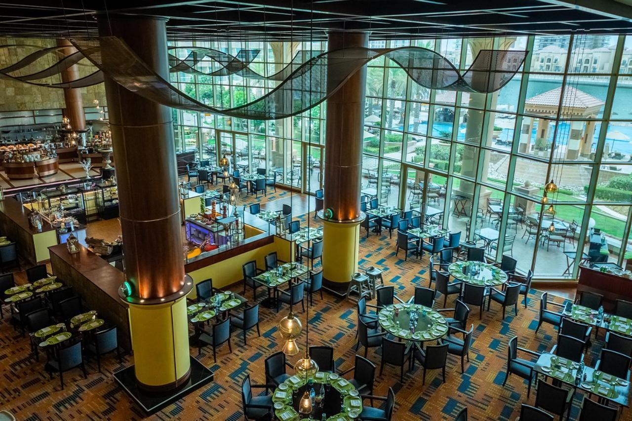 Al Raha Beach Resort & Spa Абу Даби Екстериор снимка The photo shows the interior of a restaurant with a modern design. It features large windows allowing natural light to flood the space, creating an inviting atmosphere. The dining area is furnished with round tables covered with green tablecloths and