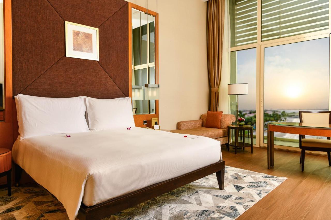 Al Raha Beach Resort & Spa Абу Даби Екстериор снимка The photo shows a stylish hotel room featuring a large bed with white bedding, positioned against a textured wall. There’s a small seating area with a chair and a table, and a window with curtains that allows natural light to fill the space. The room