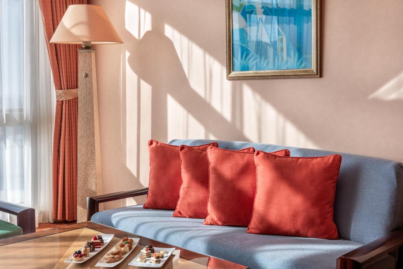 Al Raha Beach Resort & Spa Абу Даби Екстериор снимка The photo shows a cozy interior setting, likely a sitting area. It features a light blue couch with four red cushions. In front of the couch, there is a glass table displaying an assortment of snacks or small dishes. The room has soft lighting, with 