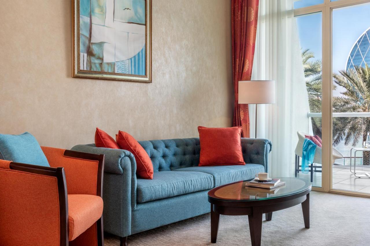 Al Raha Beach Resort & Spa Абу Даби Екстериор снимка The photo shows a well-decorated living room. There is a plush blue couch with orange accent pillows and a cozy orange armchair nearby. A round coffee table sits in front of the couch, and above it, there is a colorful painting hanging on the wall. L