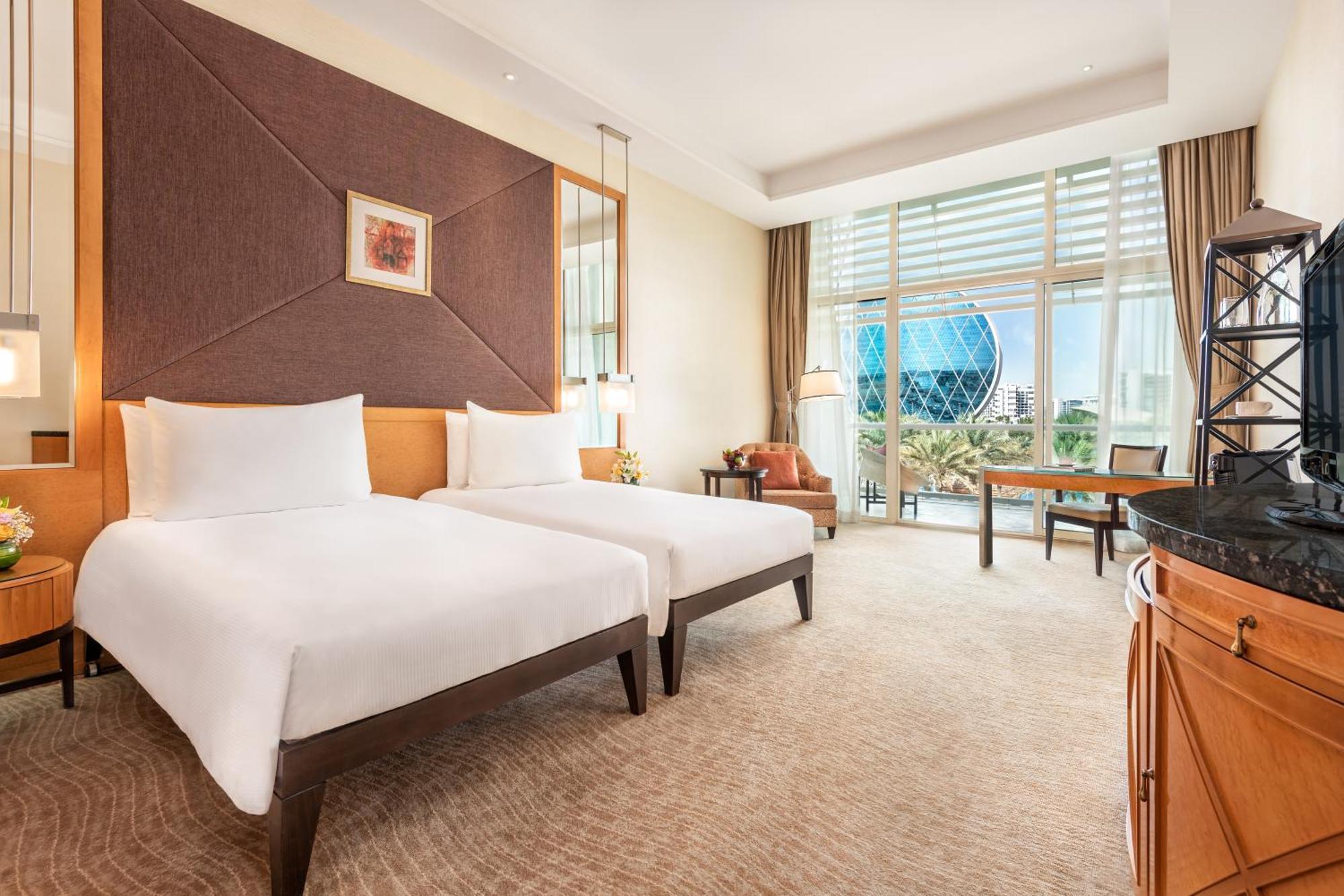 Al Raha Beach Resort & Spa Абу Даби Екстериор снимка The photo shows a well-decorated hotel room featuring two single beds with white linens. The room has a modern aesthetic, with a large window letting in natural light and offering a view of a circular structure outside, possibly a landmark or artisti