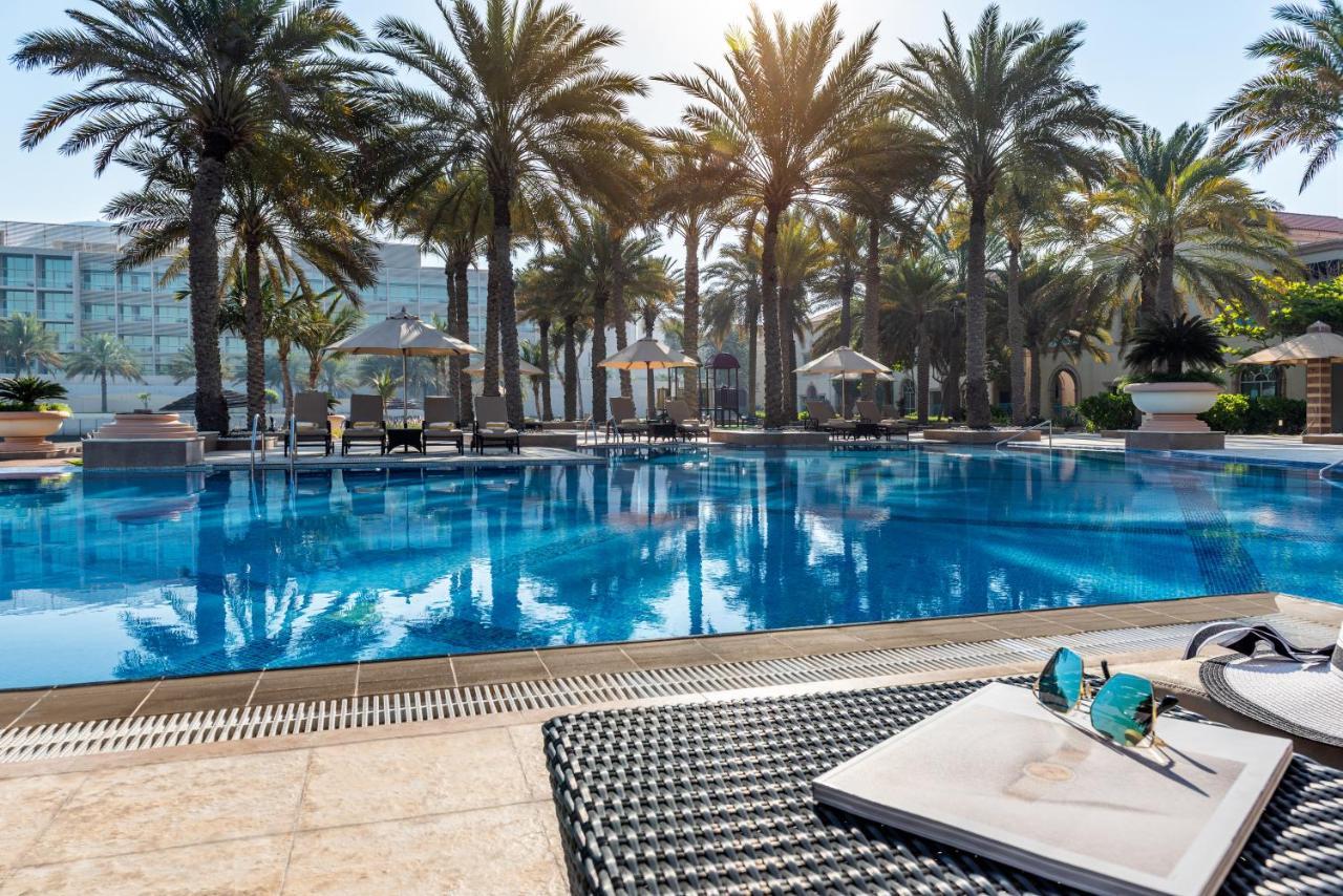 Al Raha Beach Resort & Spa Абу Даби Екстериор снимка The photo shows a vibrant swimming pool surrounded by palm trees under a clear sky. The pool's water is sparkling in the sunlight, creating a serene and inviting atmosphere. Lounge chairs are placed around the pool, some of which are shaded by umbrel