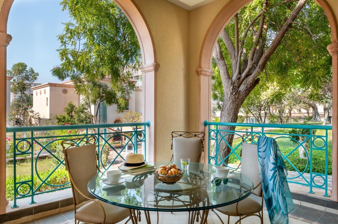 Al Raha Beach Resort & Spa Абу Даби Екстериор снимка The photo shows a serene outdoor balcony setting. There is a circular glass table with a bowl of fruit or snacks in the center, alongside a glass and a small plate. Surrounding the table are four elegant chairs. The railing is turquoise, framing a vi