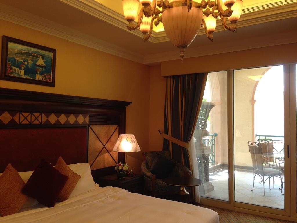 Al Raha Beach Resort & Spa Абу Даби Екстериор снимка The photo shows the interior of a hotel room. The room features a large bed with decorative cushions and a wooden headboard. There's a bedside lamp emitting a warm light, and a painting is hung on the wall above the bed. To the right, there's a windo