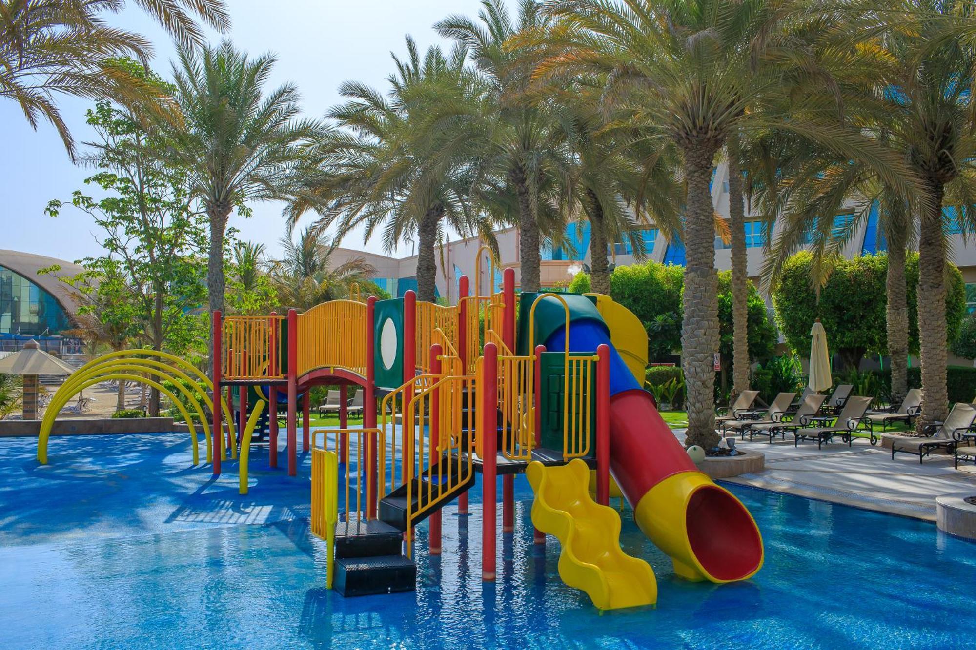Al Raha Beach Resort & Spa Абу Даби Екстериор снимка The photo shows a colorful water play area located in a pool setting. It features a variety of play structures, including slides in multiple colors, such as yellow, red, and blue. Surrounding the play structure are palm trees, creating a tropical atm