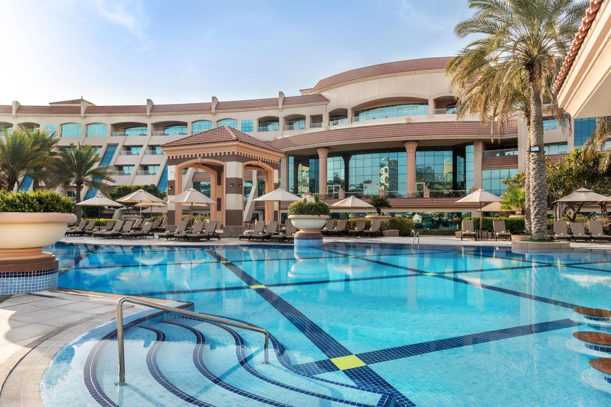 Al Raha Beach Resort & Spa Абу Даби Екстериор снимка The photo shows a luxurious resort with a large swimming pool in the foreground. The pool has a clean, blue surface and features lounge chairs on the surrounding deck. In the background, there is a stylish and modern hotel building with multiple stor