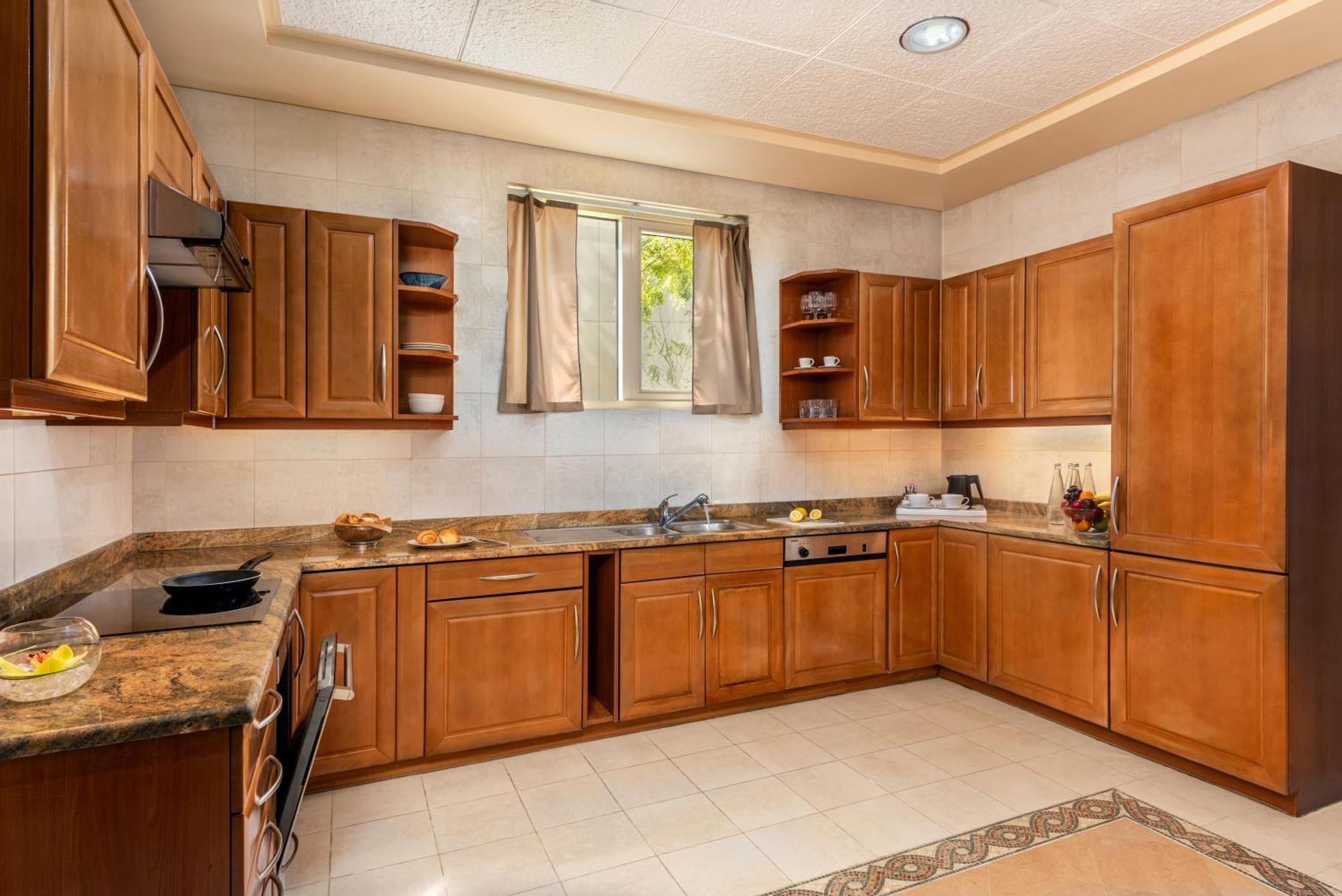 Al Raha Beach Resort & Spa Абу Даби Екстериор снимка The photo shows a cozy kitchen featuring wooden cabinets with a rich brown finish, providing a warm and inviting atmosphere. The countertops are made of a light-colored stone, complementing the cabinetry. There is a window above the sink, allowing na