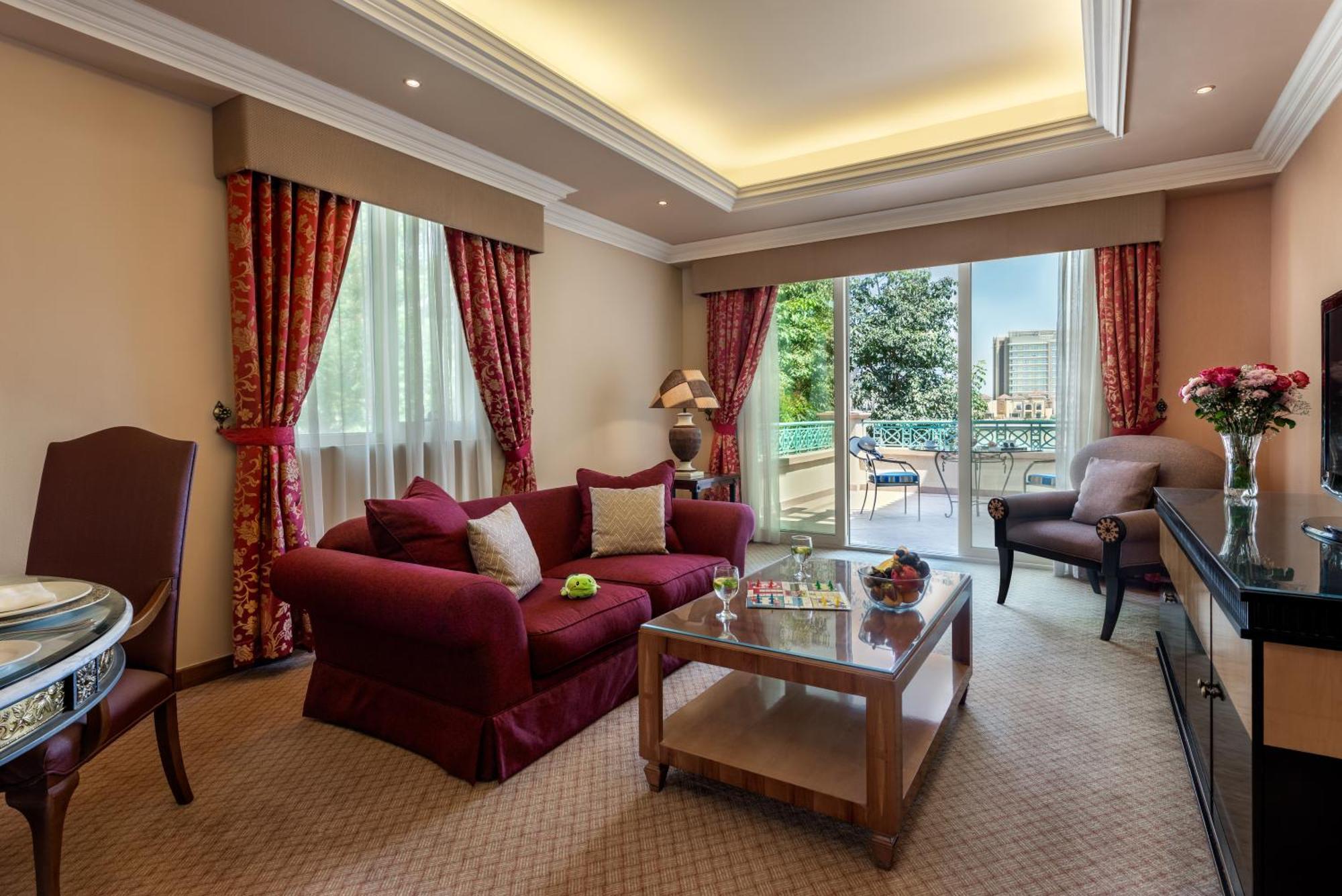 Al Raha Beach Resort & Spa Абу Даби Екстериор снимка The photo shows a well-decorated hotel room or living area. It features a cozy seating arrangement with a deep red couch adorned with cushions, paired with a single chair. There is a glass coffee table in front of the couch, which is set on a plush c