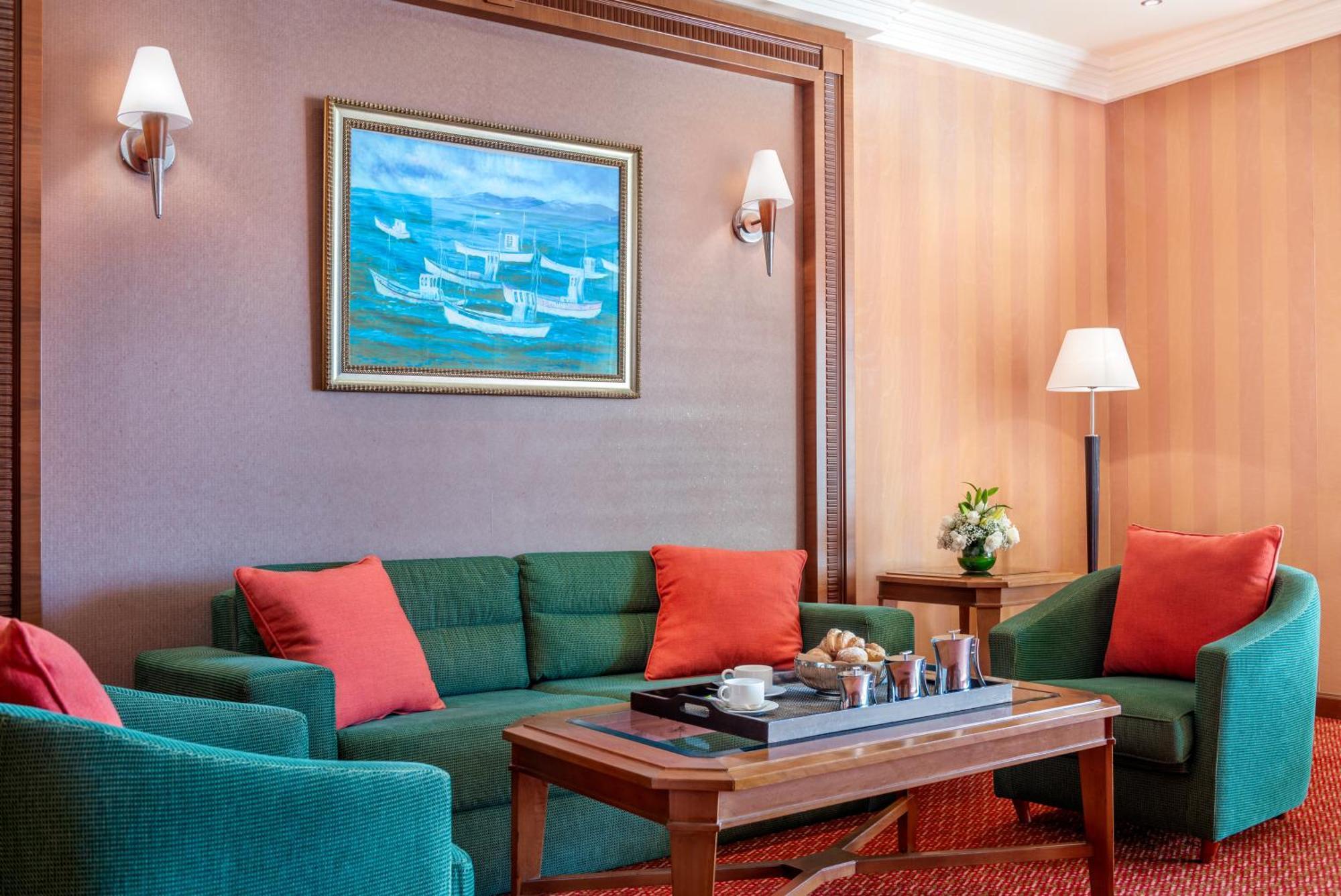 Al Raha Beach Resort & Spa Абу Даби Екстериор снимка The photo displays a cozy and elegantly furnished living area. It features a green sofa adorned with orange cushions and two matching green armchairs. A wooden coffee table sits in the center, which holds a tray with beverages and snacks. The walls a