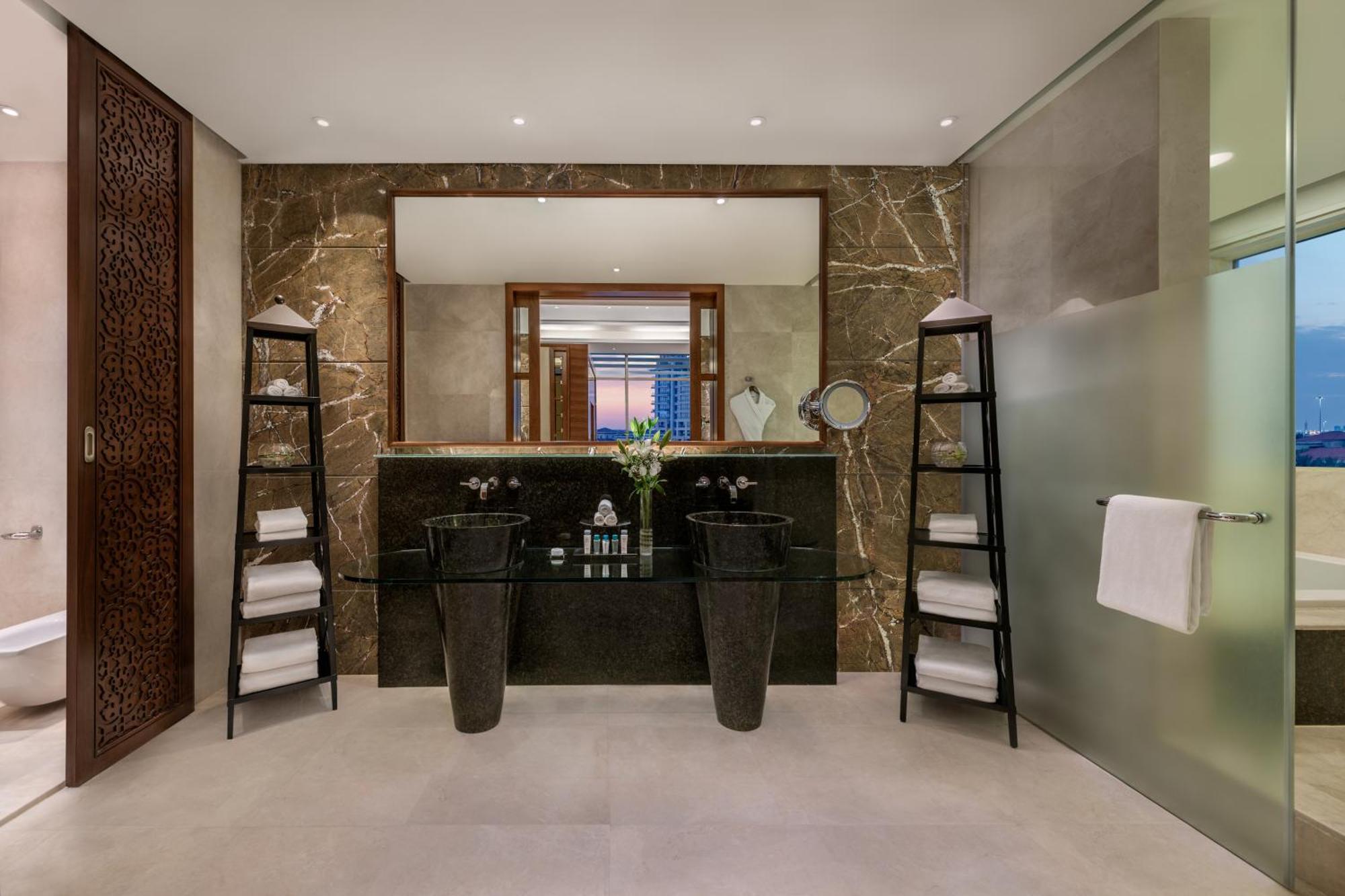 Al Raha Beach Resort & Spa Абу Даби Екстериор снимка The photo shows a modern, elegant bathroom interior. It features a large mirror hanging above a double-sink vanity with a dark stone countertop. On either side of the vanity are tall, slender vases that might be holding decorative elements. There are