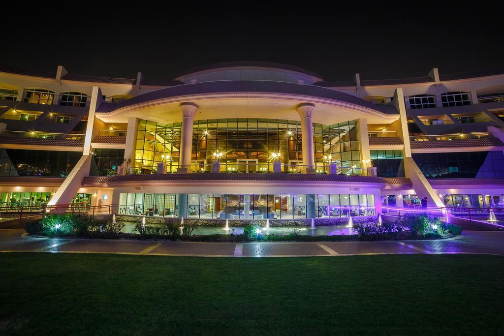 Al Raha Beach Resort & Spa Абу Даби Екстериор снимка The photo shows a modern architectural building illuminated at night. The structure has a large central entrance with multiple glass windows, flanked by symmetrical columns. The exterior features a combination of sleek lines and curves, with lighting